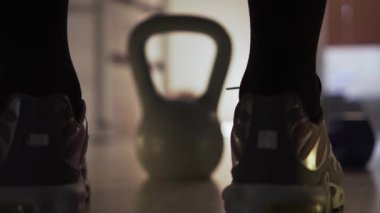 Spor salonunda, spor ayakkabılı bir adam bir kettlebell 'e doğru yürür, onu alır ve kaldırır. Spor yaptığı bir fitness merkezinde kalıyor. Arka planda birkaç dambıl ve basketbol topu var.