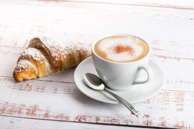 Breakfast with cappuccino and croissant on wooden table.