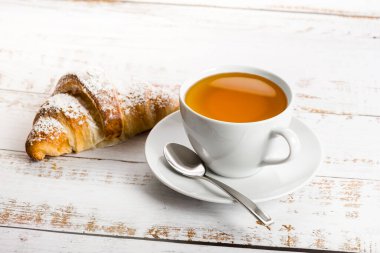 Breakfast with cup of tea and croissant on wooden table.
