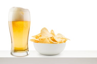Bir bardak bira ve beyaz masada patates cipsi. 