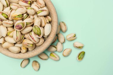 Fıstıklı fıstıklar açık yeşil arka planda ahşap kaseye konur. Üst görünüm.