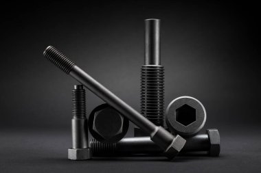 Siyah arka plandaki büyük siyah çelik vidaların çeşitliliği.