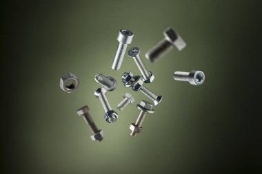 Çelik vida ve cıvataların çeşitliliği yeşil arka planda uçuyor.