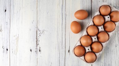 Kartonda on kahverengi yumurta ve dışarıda yukarıdan bakıldığında beyaz ahşap masa üzerinde duran iki yumurta.