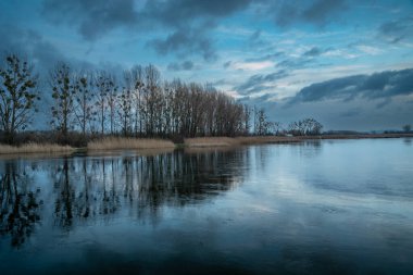 Cloudy rainy evening sky and trees reflecting in a frozen lake, Stankow, Poland