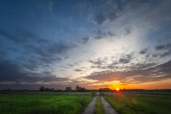 Sunset and evening clouds over meadow with dirt road, eastern Poland