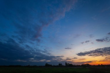 Akşam bulutları ve gün batımından sonra gökyüzü yeşil bir çayırda.