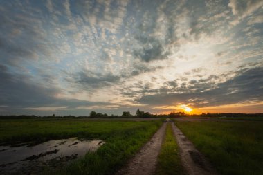 Polonya 'nın doğusunda, bahar akşamı, toprak bir yol üzerinde bulutlarla gün batımı