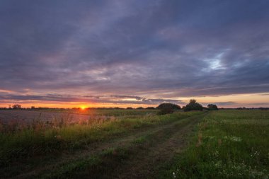 Gün batımında renkli bulutlarla tarlalar ve çayırlar boyunca kirli yollar.