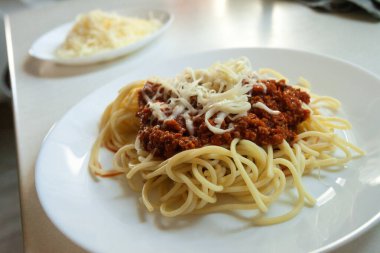 Mutfak tezgahında büyük yuvarlak bir tabakta servis edilen sarı peynirli domates soslu kıymalı makarna.