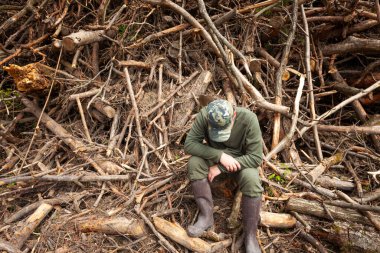 Yorgun bir orman işçisi Polonya 'nın doğusundaki ağaç kesme operasyonundan kalma bir ağaç ve kök yığınının önünde oturuyor.