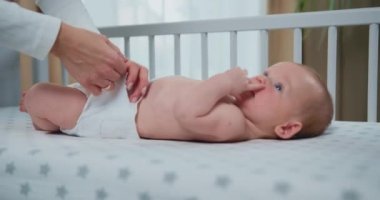 Annesi beşikte bebek bezi değiştirirken çekilmiş küçük bebek portresi, üç aylık bebek konsepti. Anne yatakta bebek bezini değiştirmiş, kadın da bebek bezini takmış. Yavaş çekim