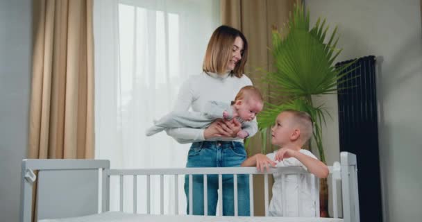 年轻的母亲抱着新生儿 站在婴儿的床边 开心地笑着的画像 刚出生的男婴又可爱又快乐 母亲的概念 慢动作 — 图库视频影像