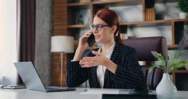 Modern ofis ile konuşan mutlu iş kadınının portresi. Kadın elinde cep telefonuyla evde oturuyor, akıllı telefonuyla müşteriye danışıyor. Yavaş çekim.