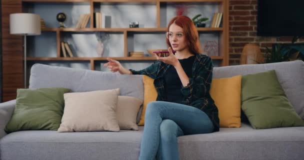 매력적 여성은 거실의 소파에 네트워크 상에서 메시지로 응답하는 스마트폰을 이용한다 — 비디오