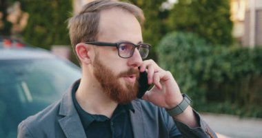 Kapatın. Başarılı bir beyaz adam cep telefonuyla konuşuyor, arabaya yaklaştı ve oturdu. Taksi servisinin erkek kullanımı. Yavaş çekim.