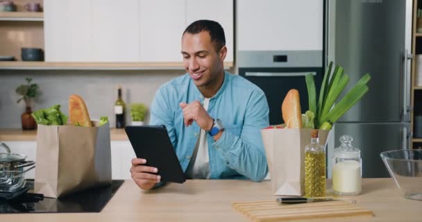 朝食中に台所でタブレットPcを使用して男 モバイルアプリ 現代のインターネットオンライン情報技術を使用してタブレットポータブルコンピュータを持つアフリカの男性 スローモーション — ストック動画
