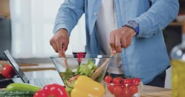 Erkek eller kaşıkları tutuyor ve sıcak mutfakta akşam yemeği için cam kasede taze sebze salatası karıştırıyor. Ev yapımı beslenme konsepti. Yavaş çekim