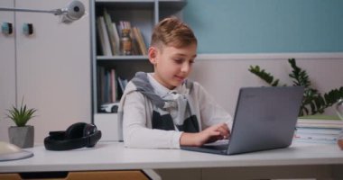Çocuk çalışmak için dizüstü bilgisayar kullanıyor, online dersler, atölyeler ve yüksek lisans dersleri izliyor. Modern odadaki dizüstü bilgisayar derslerine katılan zeki çocuk. Yavaş çekim.