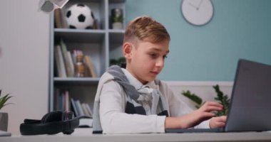 Gülümseyen küçük çocuk internet sitesinde arkadaşlarıyla sohbet ediyor. Evdeki oturma odasında oturan dizüstü bilgisayarla çocuk öğrenme portresi. Yavaş çekim.