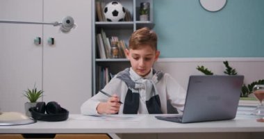 Modern çocuk ev ödevini yapıyor ve dizüstü bilgisayarının önünde oturuyor. Çocuk dijital tablet kullanıyor, video dersinde öğreniyor. Yavaş çekim.