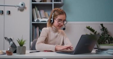 Smart 10 years old caucasian schoolgirl using laptop wearing earphones has online lesson, video call, , raises his hand to answer the question. Cute child has distance studying at home using laptop