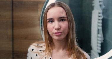 Closeup portrait of attractive blond woman with natural makeup with perfect wrinkled face skin care spa procedures looking at camera in bathroom. Slow motion.