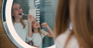 Funny girls is singing and dancing in bathroom wearing pajamas having fun alone at home. Sisters in front of the mirror holding a toothbrush dances and sings. Slow motion.