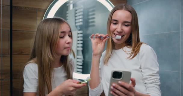 Młode Uśmiechnięte Dziewczyny Używają Smartfona Podczas Mycia Zębów Pastą Zębów — Wideo stockowe
