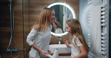 Joyful young woman and little girl in a white robe dries her hair, sings and dances in the bathroom at home. Caucasian girls in playful mood after shower. Slow motion.