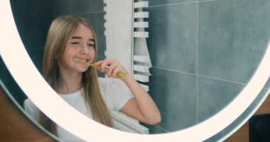 Portrait happy cute young teenage girl brushing teeth in bathroom and smiling at home. Children daily healthcare routine. Caucasian kid with white tooth looking at mirror. Slow motion.