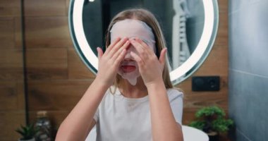 Teenager kid skin care treatment, natural cosmetics. Lovely young smiling child girl applying cosmetic moisturizing face mask. Slow motion.