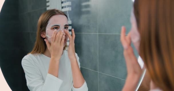 Mujer Joven Sonriente Tomando Máscara Hidratante Cara Mirando Espejo Baño — Vídeos de Stock