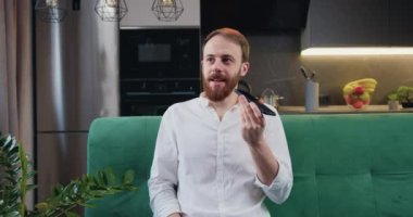 Attaractive man sit in kitchen hold smart phone talk on speakerphone. Male recording audio message for friends or partners, sharing news using mobile phone application.