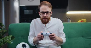 Middle age smilling man playing video game in moderm kitchen apartment enjoying indoor activity. Online entertainment and leisure activity concept.
