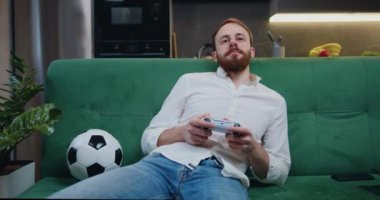 Middle aged man reacting to loss in video game at home. Young sad male using controller having loss on video game on sofa in modern kitchen. Slow motion.