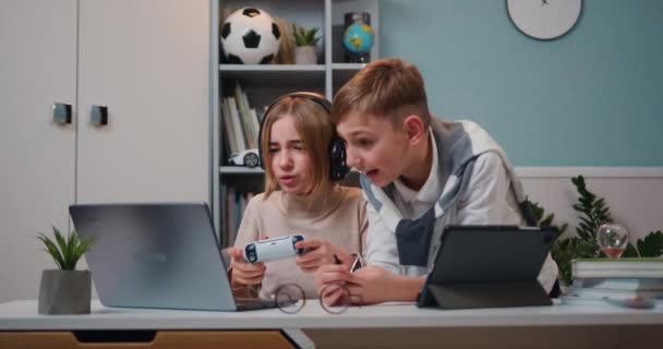興奮した白人のゲーマーの女の子と若い男の子がテーブルに座って コンソールでビデオゲームをプレイします 子供はワイヤレスコントローラで再生します スローモーション — ストック動画