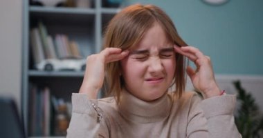 Evde arka plandaki kitaplıkta geçirdiği yorucu bir günün ardından baş ağrısıyla şakaklarına dairesel hareketlerle masaj yapan yorgun ergen kızın yüzünü kapat. Yavaş çekim
