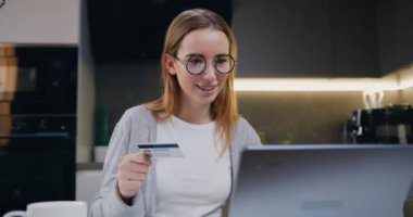 Bir kadın online bir mağazadan alışveriş yapmak için kredi kartını kullanıyor. Evde banka kartı ve dizüstü bilgisayar kullanarak online alışveriş yapan güzel sarışın bir kız. Yavaş çekim.