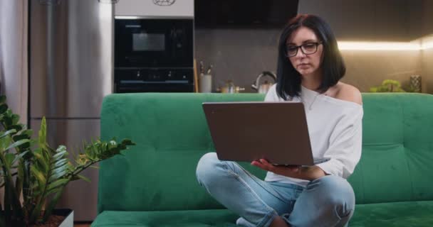 自宅の緑のソファに座っている間 コンピュータを使用して目の中に思慮深い若い白人女性 ネットをサーフィン スローモーション — ストック動画