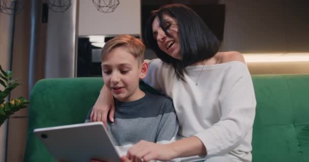 年轻的高加索女人和她可爱的小儿子一起使用平板电脑 在家里玩得很开心 有爱心的年轻妈妈和儿子呆在家里 男孩和妈妈一起在家里看社交视频 — 图库视频影像