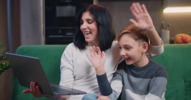 9 yaşında tatlı bir çocuğu olan güzel bir kadın elinde dizüstü bilgisayarla kanepede oturup ailesiyle görüntülü konuşma yapıyor. Mutlu aile ve modern teknoloji. Yavaş çekim