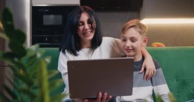 Evde dizüstü bilgisayar kullanan oğluyla güzel bir kadın. Mutlu anne ve anaokulu çocuğu kanepede oturup internetten çizgi film izliyor ya da video oyunu oynuyorlar. Neşeli bir aile. Yavaş çekim
