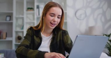 Çekici, güler yüzlü, modern sarışın kadın evdeki masada oturmuş arkadaşlarıyla bilgisayar başında sohbet ediyor. Yavaş çekim.