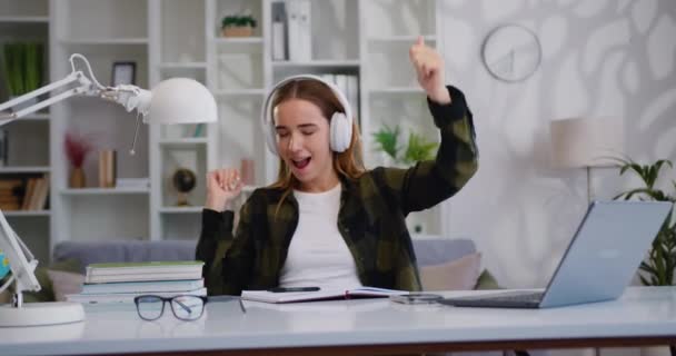 stock video Young woman listening music and singing in headphones and dancing, networking on laptop. Emotional female portrait. Female carefree listening to music in modern headphones. Slow motion.