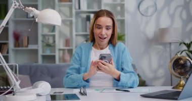 Mutlu bir kadının portresi akıllı telefon daktilo kullanarak harika bir kazanç yakaladı. İyi haber, zaferi sınıf dairesinde kutlayın. Neşeli kız telefonda iyi haberler okuyor. Yavaş çekim.