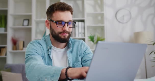 リビングルームの机の後ろに座っている間 ノートパソコンで働くハンサムな原因者 フリーランスの男性専門家が自宅から仕事から重要な電子メールを書いています スローモーション — ストック動画