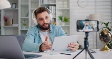 Blogcu, oturma odasındaki tripoda akıllı telefondan yeni bir eğitim videosu kaydediyor. Yayınlanan iletişim podcast etkinliği, uzaktan danışma konsepti. Yavaş çekim.