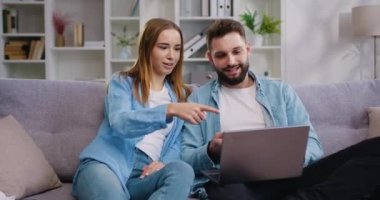 Oturma odasındaki kanepede dinlenirken gülümseyen kadın ve erkek evlerinde komik videolar ya da internetten filmler izliyorlar. Yavaş çekim.
