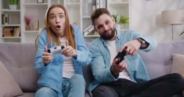Mutlu yetişkin adam ve kadın video oyunu oynayıp birlikte gülüyorlar. Evde video oyunu oynayan heyecanlı, genç, yetişkin oyuncular. Yavaş çekim.